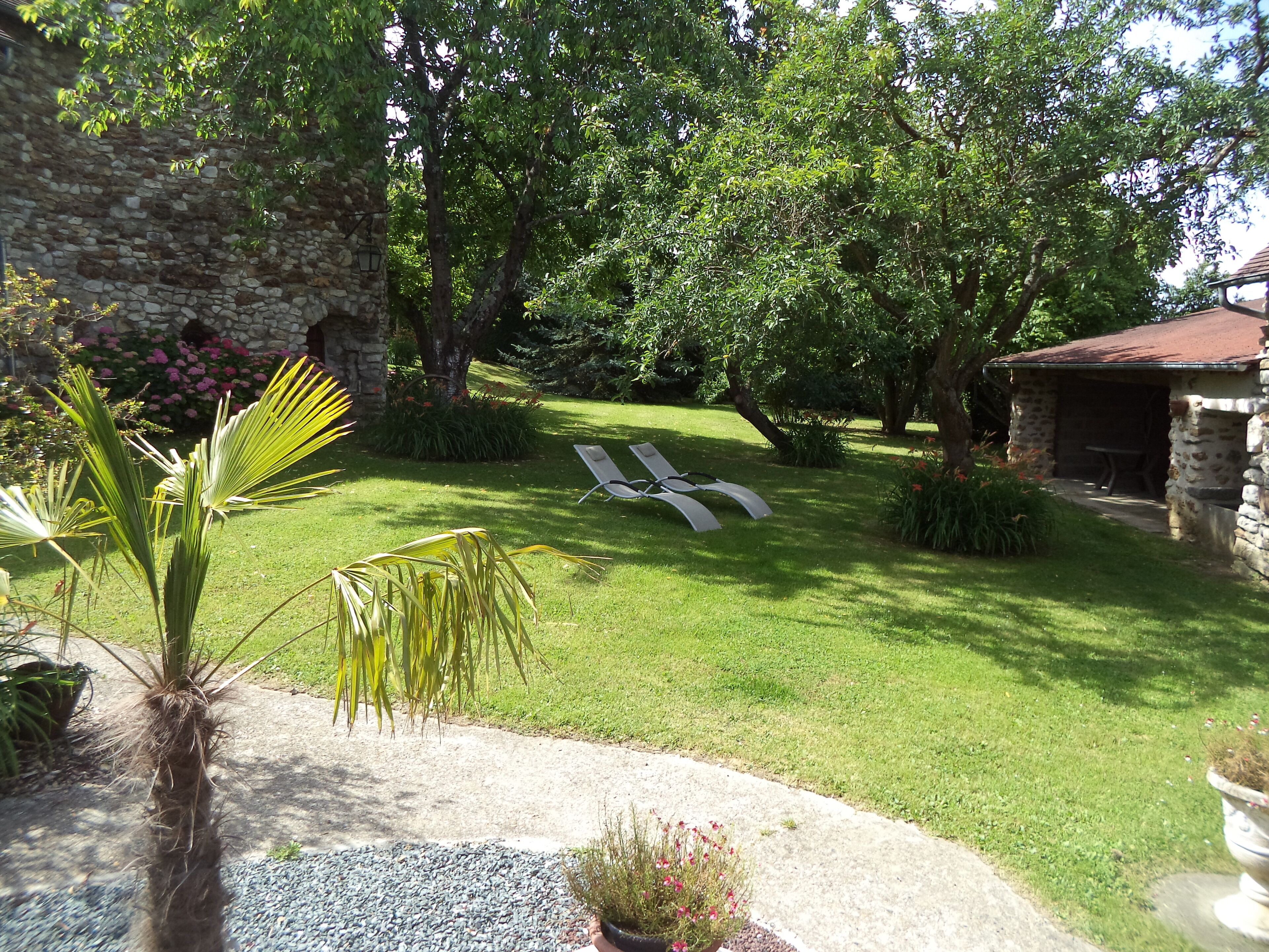 A well-maintained garden with a stone wall, a lawn with two lounge chairs, and a small stone building.