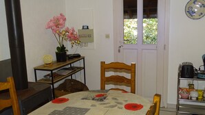 Une cuisine chaleureuse avec une table à manger, des chaises, une plante en pot et une fenêtre donnant sur un paysage verdoyant.