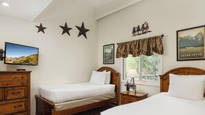Une chambre d’hôtel avec deux lits simples, une commode en bois, un téléviseur à écran plat et une fenêtre donnant sur les montagnes.
