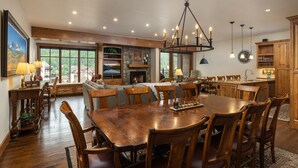A spacious dining area with a large wooden table and chairs, a chandelier, and a fireplace.