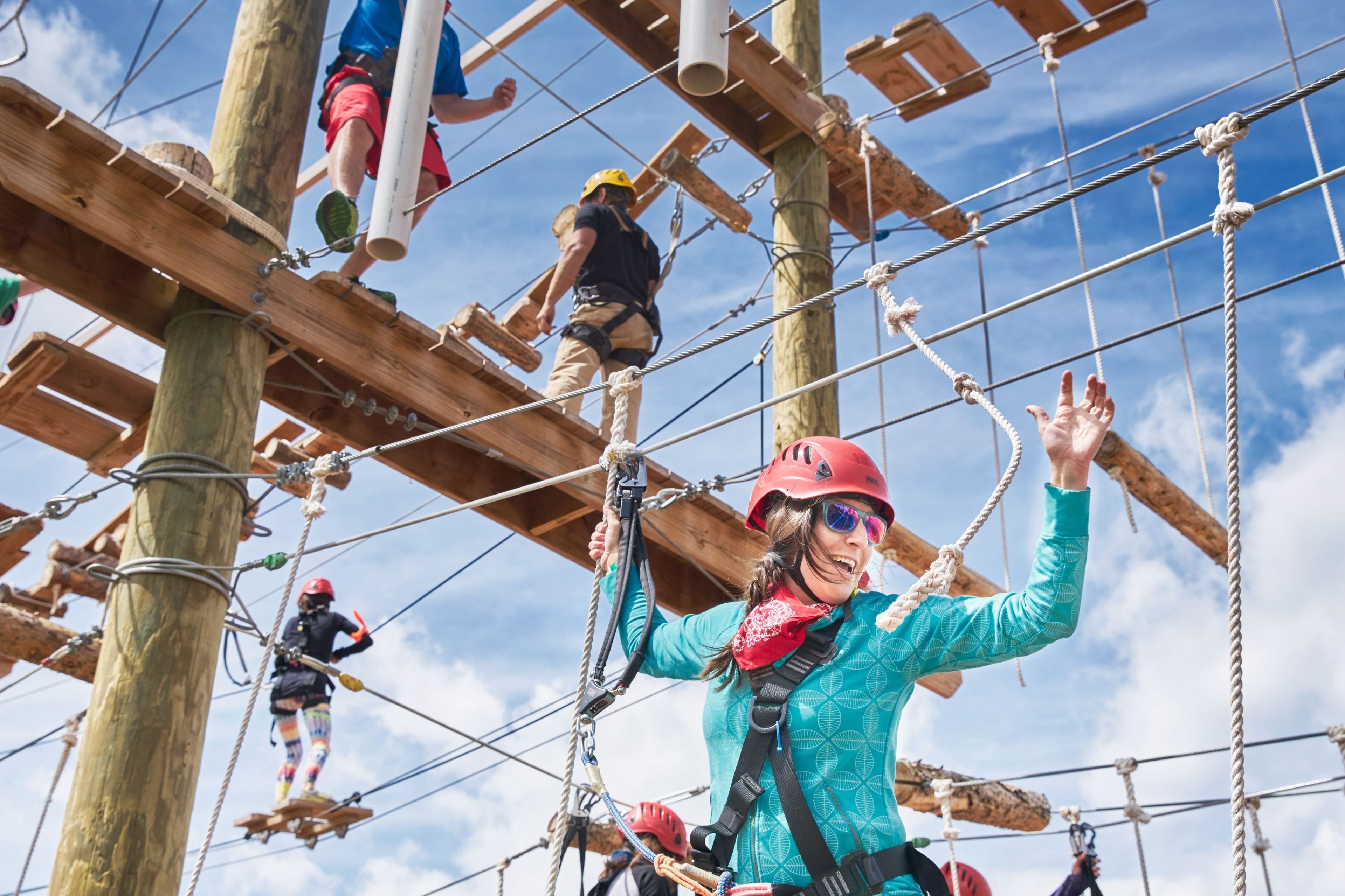 A group of people engaged in an outdoor adventure activity, navigating through a wooden obstacle course with ropes and platforms.