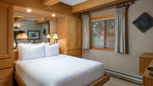A neatly made bed in a room with wooden paneling, a window with blinds, and a wall-mounted artwork. - Vantage Point 115 - 2 Bedroom Gold (Circle Vail)