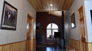 A wooden interior with a high ceiling, a chandelier, wooden benches, and a view through an arched window.