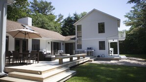 Ein zweigeschossiges Haus mit Terrasse, Gartenmöbeln und Grill.