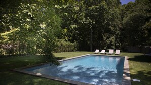 Ein rechteckiger Pool mit gefliestem Rand, umgeben von einem gepflegten Rasen und Bäumen.