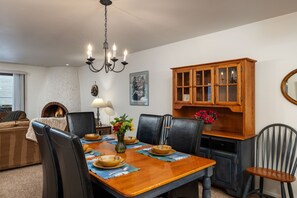 Un comedor con mesa de madera, sillas, candelabro, chimenea y aparador con puertas de vidrio.