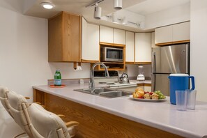 A modern kitchen with wooden cabinets, stainless steel appliances, a sink, and a breakfast bar. - Enzian 115 - Lionshead Vail 3BR, Minutes to Gondola + Valley Views (Vail)