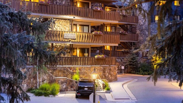 Un hôtel à plusieurs étages, doté d’une façade en pierre, de balcons en bois et d’une voiture garée devant.