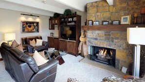 A living room with a stone fireplace, leather sofa, and a television. - Landmark 304 - 2 Bedroom Platinum (Vail)