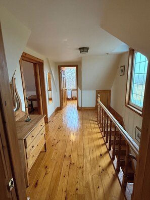 A spacious hallway with wooden flooring, a staircase, and a window providing natural light.