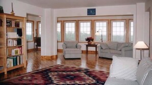 A spacious living room with a large window, a bookshelf, a patterned rug, and a sofa. - Large Century Home with Vineyard. Very private with a grand ocean view.  (Lot 63)