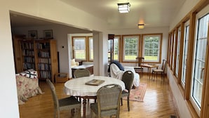 A spacious room with a dining table, chairs, a bookshelf, and large windows. - Large Century Home with Vineyard. Very private with a grand ocean view.  (Lot 63)