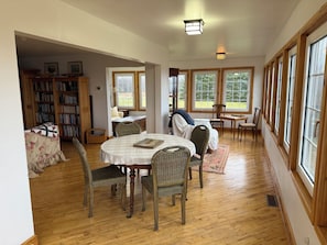 A spacious room with a dining table, chairs, a bookshelf, and large windows.