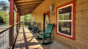 A wooden cabin with a porch, numbered 1722, featuring a wooden deck, green chairs, and a view of the surrounding forest. - Large 3 bedroom cabin.   (Sevierville)