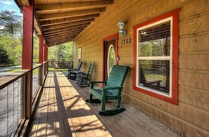 Sit on the porch and enjoy the view from this charming cabin, featuring a cozy seating area with rocking chairs and a window with a metal grill.