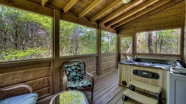 A covered deck with wooden beams, a hot tub, and a chair with a floral cushion. - Large 3 bedroom cabin.   (Sevierville)