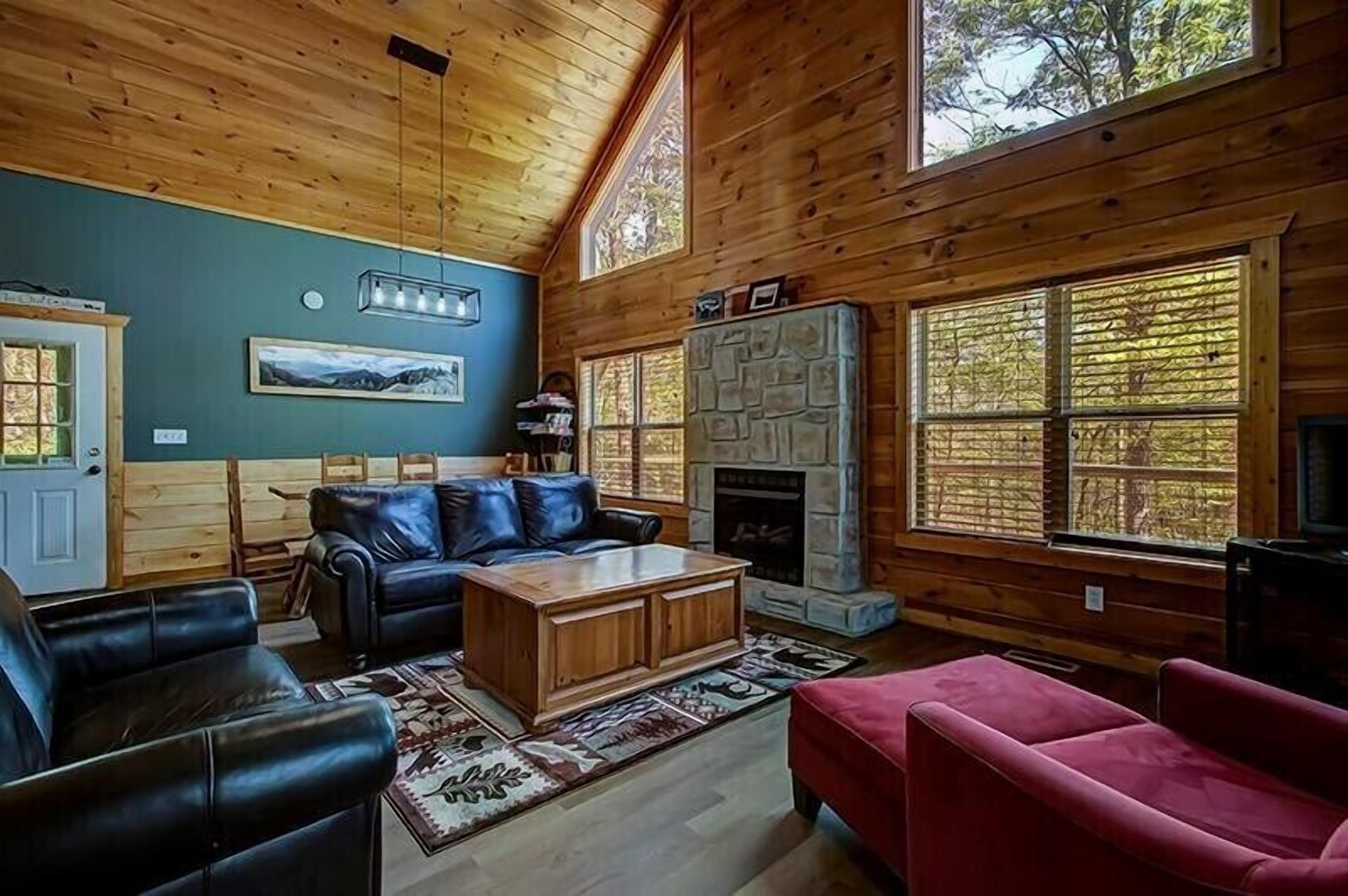 L’intérieur d’une cabane en rondins, avec une cheminée, des meubles en cuir et de grandes fenêtres.