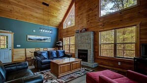 A log cabin interior with a fireplace, leather furniture, and large windows. - Large 3 bedroom cabin.   (Sevierville)