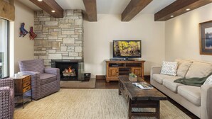 Un salon chaleureux avec une cheminée en pierre, des poutres en bois, un téléviseur et des sièges confortables.