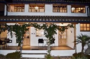 A two-story building with a covered patio area featuring wooden furniture and a small garden.