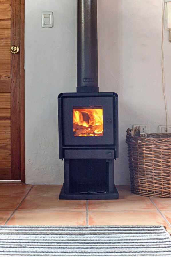 A wood-burning stove with a visible fire, a wicker basket, and a tiled floor. - Suite Sol with beautiful gardens In Historical Quito (Quito)