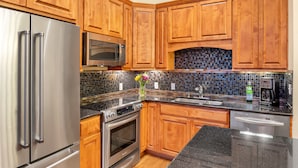 A kitchen with wooden cabinets, stainless steel appliances, a tiled backsplash, and a granite countertop.