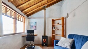 A cozy living room with a blue sofa, a round coffee table, a black chair, a bookshelf, and a wood-burning stove. - Studio Mariposa with beautiful gardens in Historical Quito (Quito)