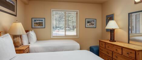 A hotel room with two beds, a wooden dresser, and a window with blinds.
