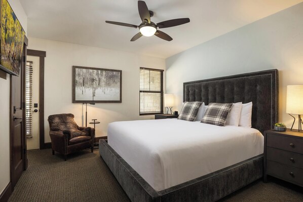 A hotel room with a large bed, a chair, a ceiling fan, and artwork on the walls.
