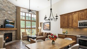 A spacious living room with a fireplace, a dining area with a wooden table, and a kitchen with wooden cabinets and a built-in oven. - Landmark 220 - 3 Bedroom Platinum (Vail)