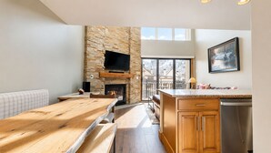 Une cuisine moderne avec une cheminée en pierre, une table à manger en bois et une grande fenêtre offrant une vue imprenable.