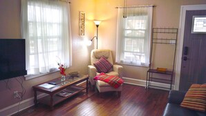 A living room with a flat-screen TV, a glass coffee table, a leather armchair with a plaid throw blanket, and a standing lamp. - CORNER OF CALM IN THE ♥ OF CEDAR RAPIDS! (Cedar Rapids)