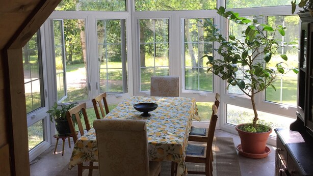 Uma estufa com mesa e cadeiras, ladeada por amplas janelas que dão para um jardim.
