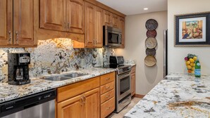 A kitchen with wooden cabinets, a stainless steel dishwasher, a microwave, and an oven. There is a marble countertop and a sink. - Landmark 401 - 2 Bedroom Platinum (Vail)