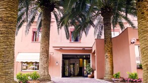 A building entrance with a paved pathway, palm trees, and potted plants. - Hotel Palme (Monterosso al Mare)