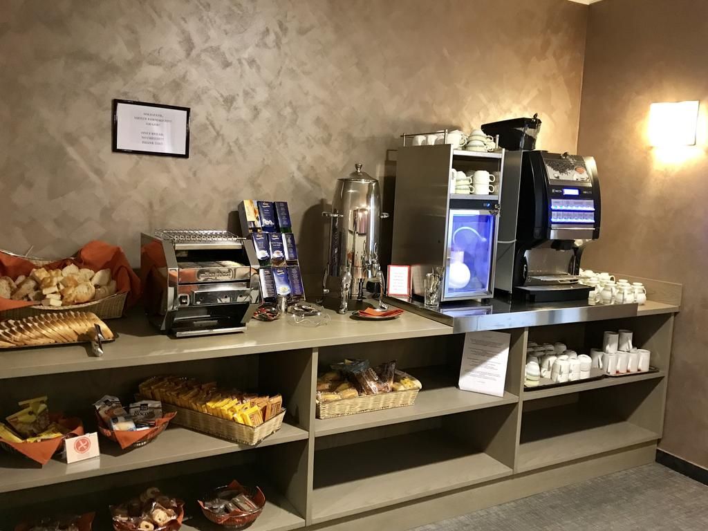 Una estación de desayuno autoservicio con cafeteras, una variedad de pasteles y un dispensador de café.