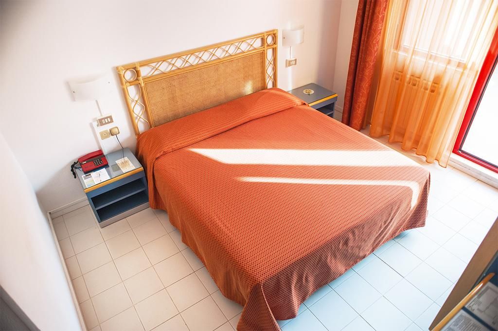 A bed with a headboard, a bedside table with a lamp, and a window with curtains.