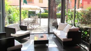 A modern indoor-outdoor living space with a glass wall, a sofa set, a coffee table, and a dining area with chairs and an umbrella. - Hotel Palme (Monterosso al Mare)