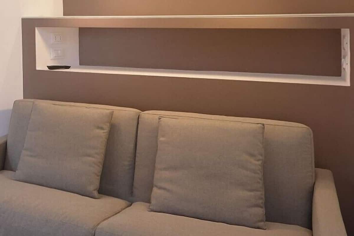 Een beige bank met twee kussens tegen een muur met een plank erboven.