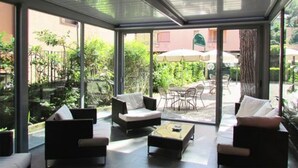 A conservatory with a glass ceiling, furnished with sofas and a coffee table, overlooking a patio area with outdoor seating and greenery. - Hotel Palme (Monterosso al Mare)