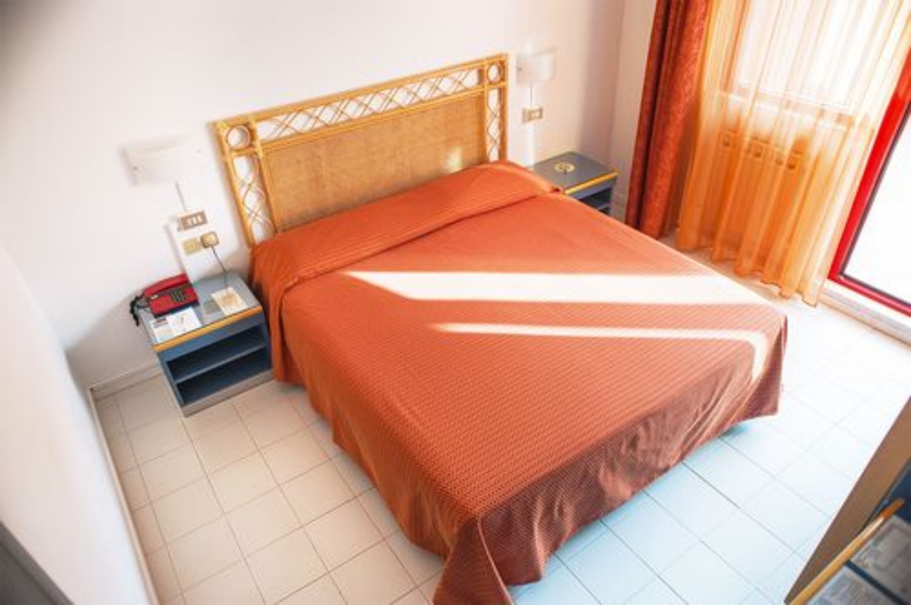 A neatly made bed with a wooden headboard, a bedside table with a lamp, and a window with curtains.