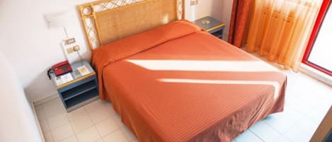 A neatly made bed with a wooden headboard, a bedside table with a lamp, and a window with curtains.