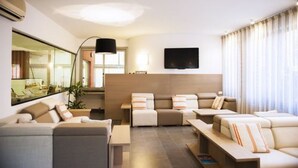 A modern living room with a sofa set, a flat-screen TV, and a large window with curtains. - Hotel Palme (Monterosso al Mare)