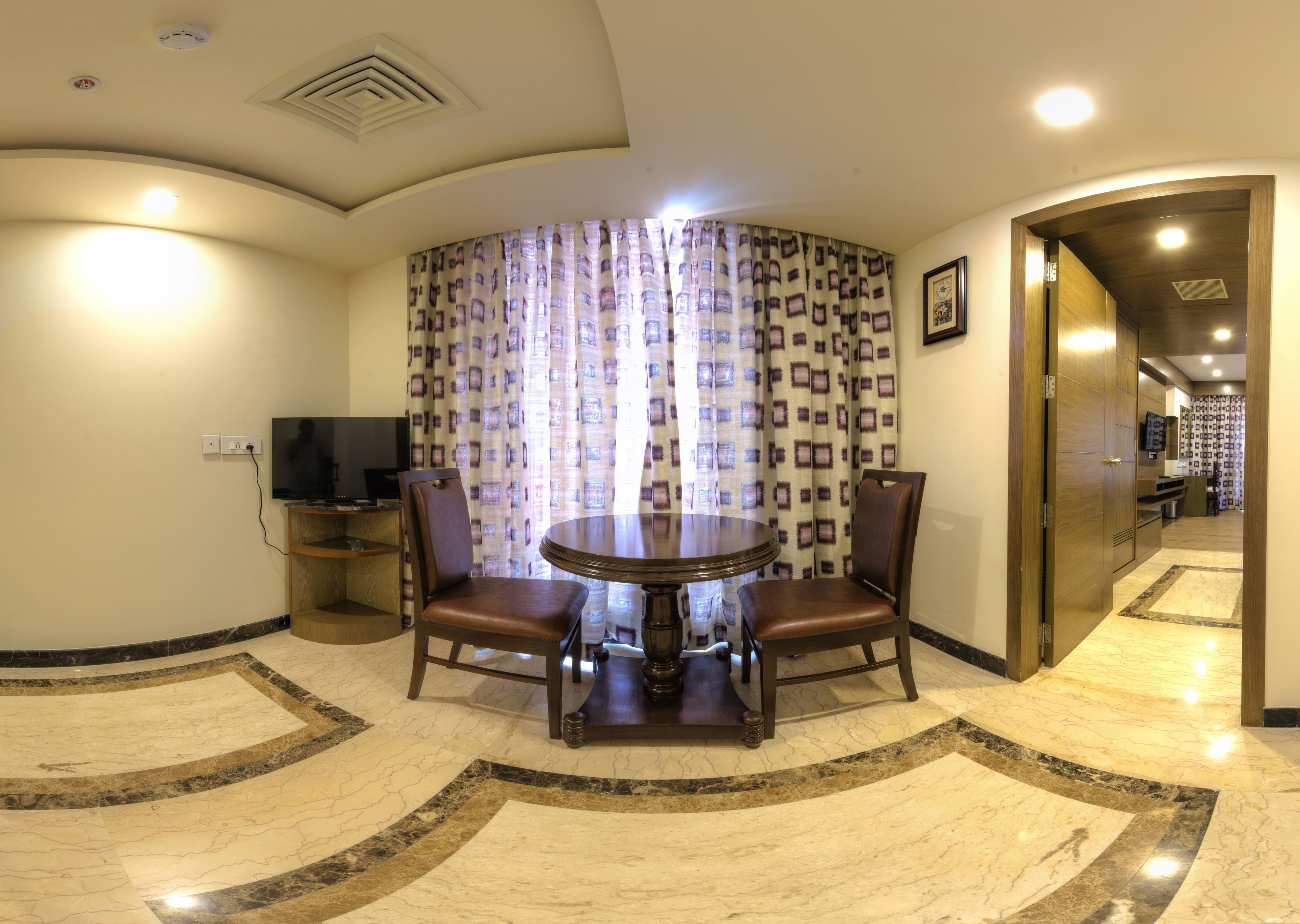 A dining area with a marble floor, a round table, two chairs, a television, and patterned curtains.