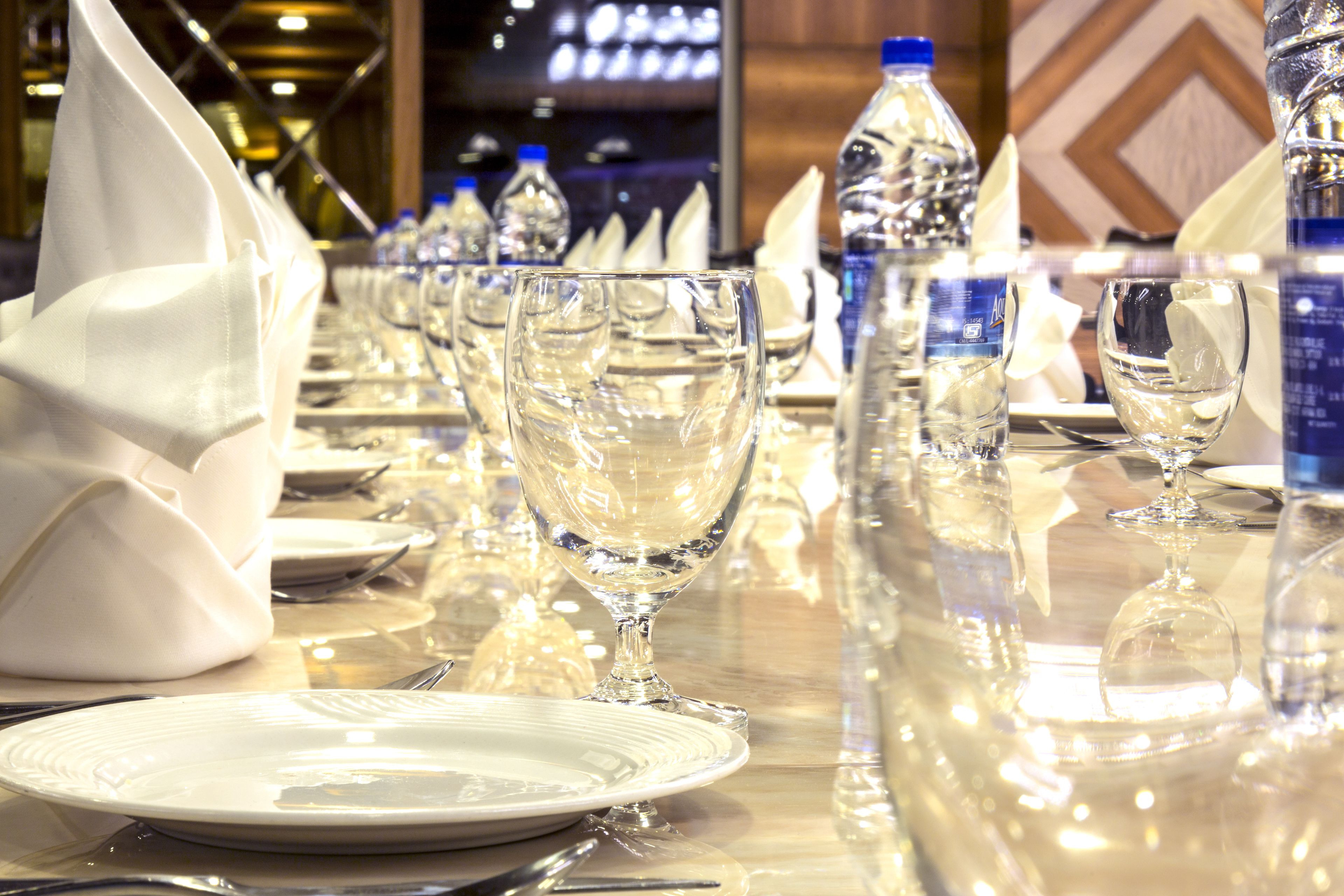 Una mesa de comedor elegantemente dispuesta, con varias copas de vino, platos y cubiertos, además de botellas de agua.