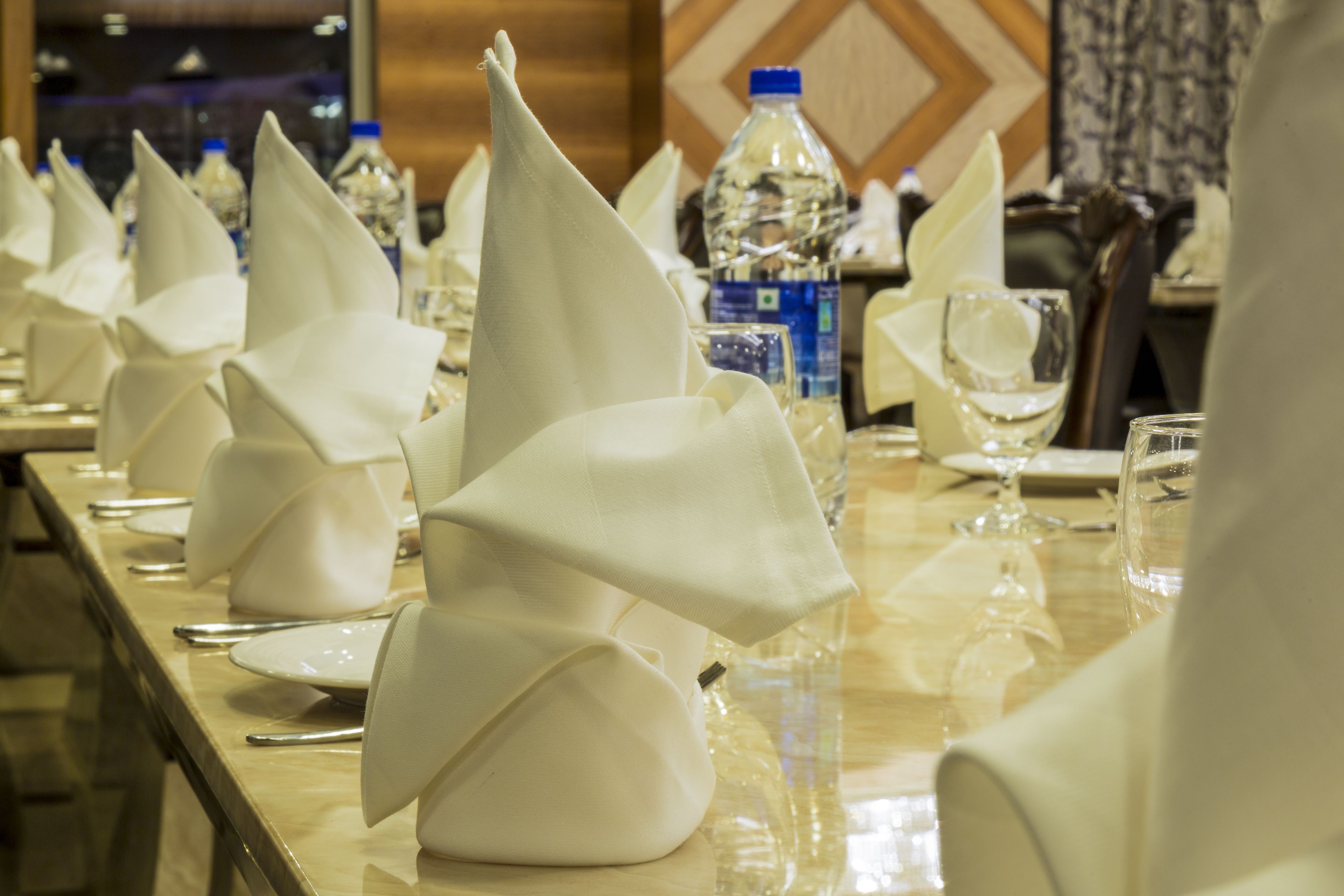 Mesa de banquete posta com guardanapos brancos dobrados em formato de barco, garrafas de água e copos.