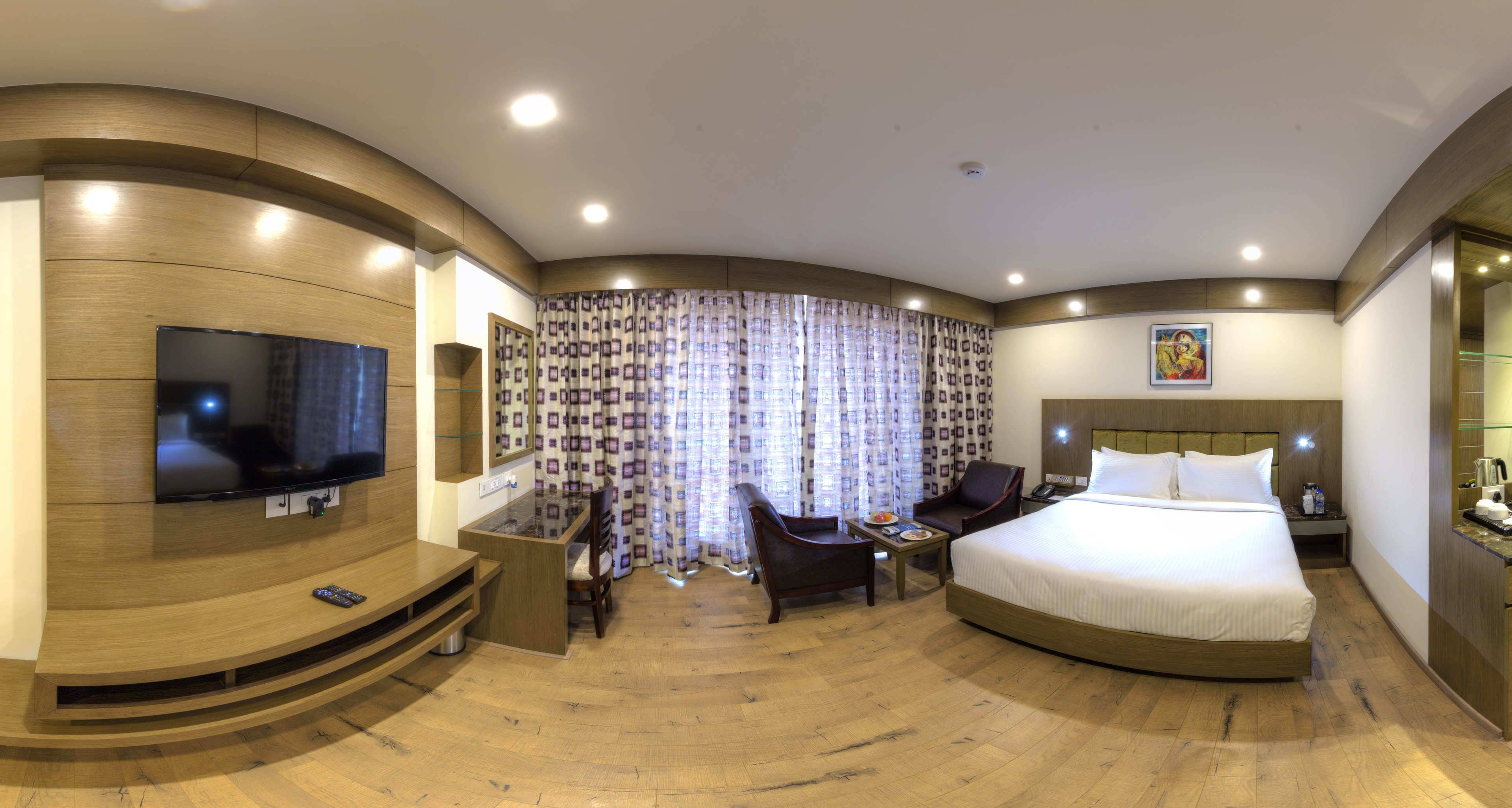 A hotel room with a curved wooden wall, a flat-screen TV, a bed, a desk, and a chair.