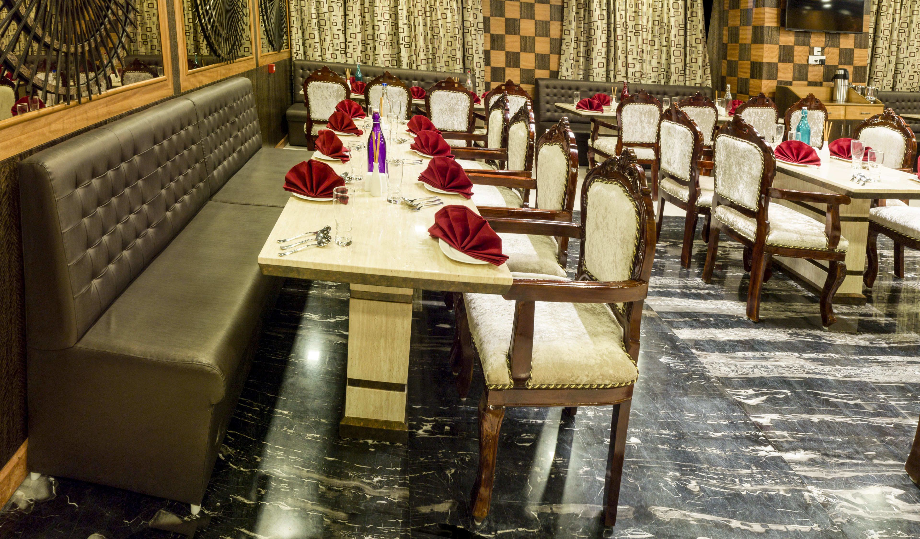 A restaurant with a long dining table set with red napkins, white plates, and silverware. There are cushioned booths and wooden chairs.
