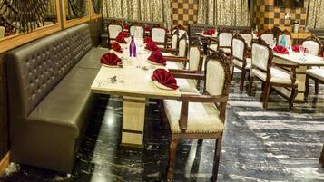 A restaurant with a long dining table set with red napkins, white plates, and silverware. There are cushioned booths and wooden chairs.