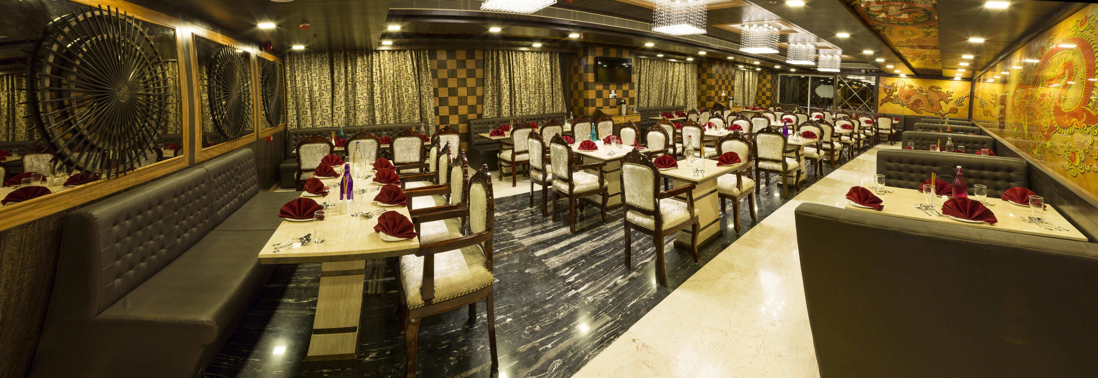 A spacious restaurant with multiple dining tables and booths, marble flooring, and a decorative wall with a dragon mural.